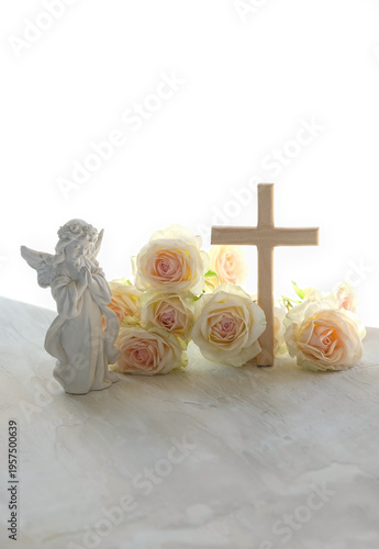 Religion background. Beautiful angel figurine with wooden cross and rose flowers on table close up. symbol of Easter holiday, Christianity religion, faith in God, prayer, memory. soft focus