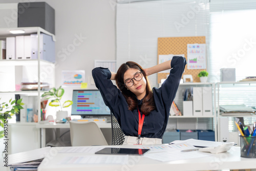 Asian business woman stretching arms at office desk with relaxing expression after work finished. Happy feeling satisfied for successful job done freelance people lifestyle break time at home office