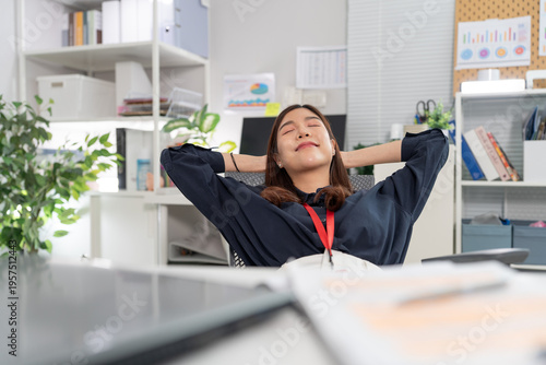 Happy Asian business woman relaxing with hands behind head leaning back on chair at office. Successful female taking break feeling relaxed and satisfied with work finished in modern workplace