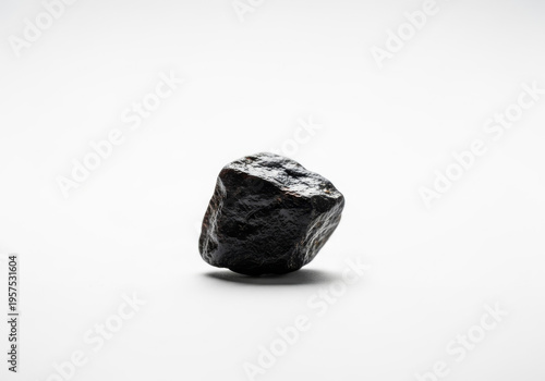 A single, rough, dark, natural shilajit resin rock isolated on a clean white background, showcasing its raw, mineral-rich texture and organic form in a minimalist studio shot.