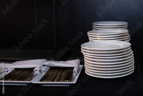 Stack of clean plates and cutlery ready for service in a restaurant setting during dinner time