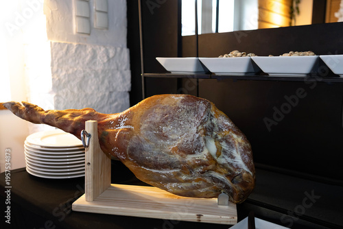 Ham leg displayed on a wooden stand in a restaurant setting with plates and nuts nearby