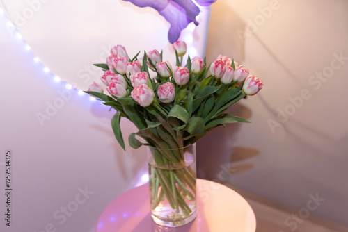Flowers in a vase on a small table with lights in the background during a gathering in a cozy indoor space