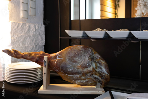 Cured ham on display at a food event near a serving table with plates and dishes in the background