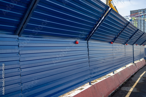 Blue metal construction fence with safety lights along the sidewalk
