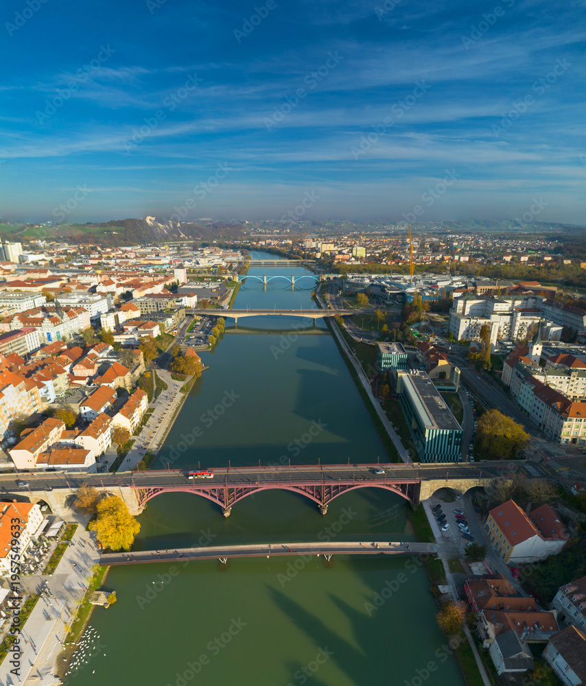 Obraz premium Aerial view of Maribor city with Drava river and multiple bridges, Slovenia. Scenic European cityscape with historic architecture and river flowing through urban landscape.