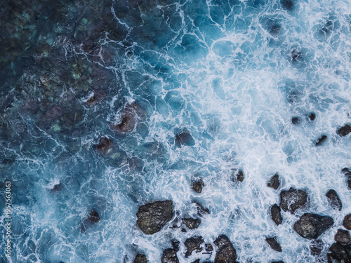 Bild auf Leinwand Aerial top-down view of turquoise ocean waves crashing against a rugged rocky shoreline