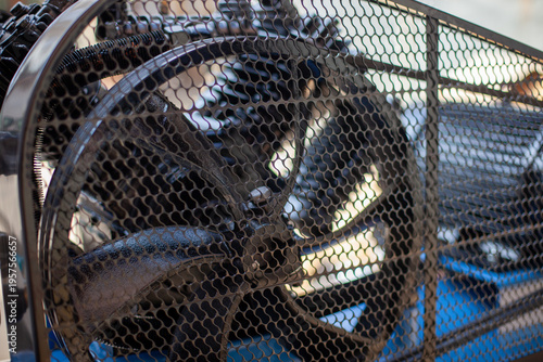 Tablou pe pânză Industrial belt drive system with pulley and v-belt protected by a black metal safety mesh guard for air compressor power transmission and occupational safety compliance in factory workshops