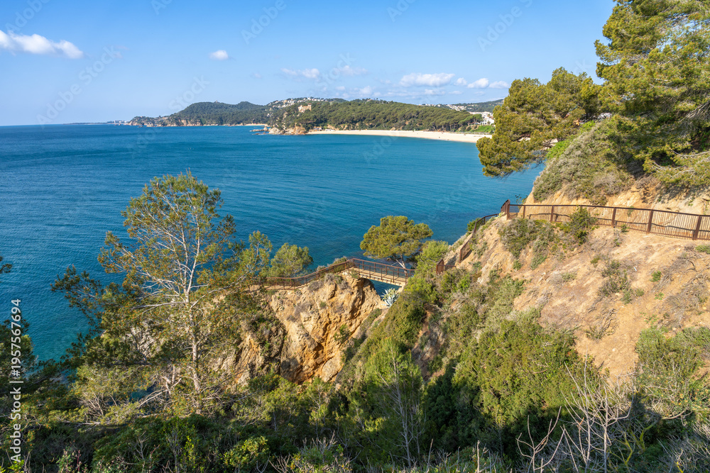 Naklejka premium Scenic coastal path winding along a rugged cliffside offering breathtaking panoramic views of fenals beach and the deep blue mediterranean sea under a clear sky