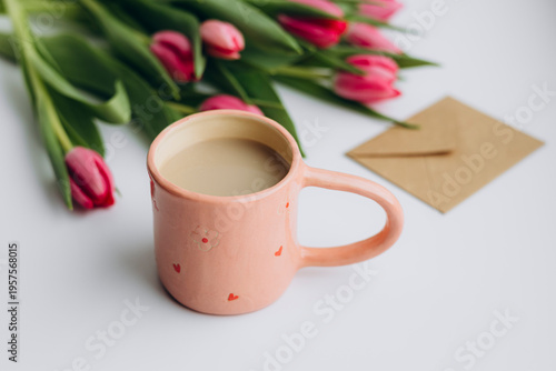 Pink mug with coffee, tulips and greeting card for holiday celebration.
