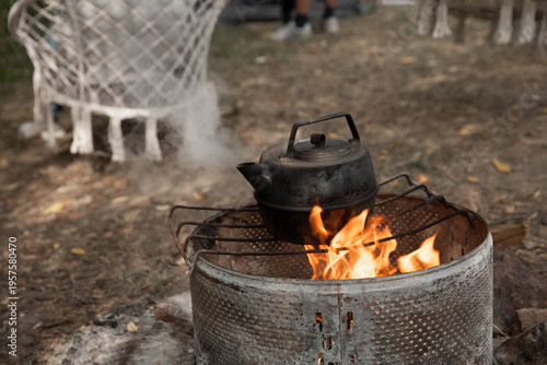the kettle on a fire  at a campsite against the background of a hanging chair during daylight hours