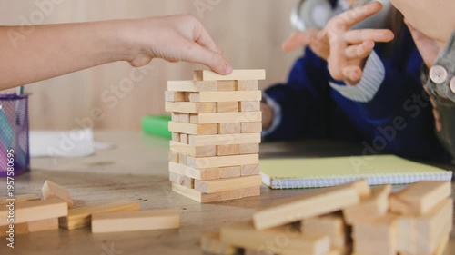 Children play a stacking game with wooden blocks at a table during a group activity in a classroom setting in the afternoon