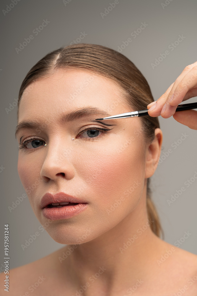 Fototapeta premium Captivating young woman applies makeup with precision in a serene beauty studio