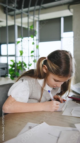 Young girl studies and writes at a table in a bright room with plants and natural light during the day,vertical video