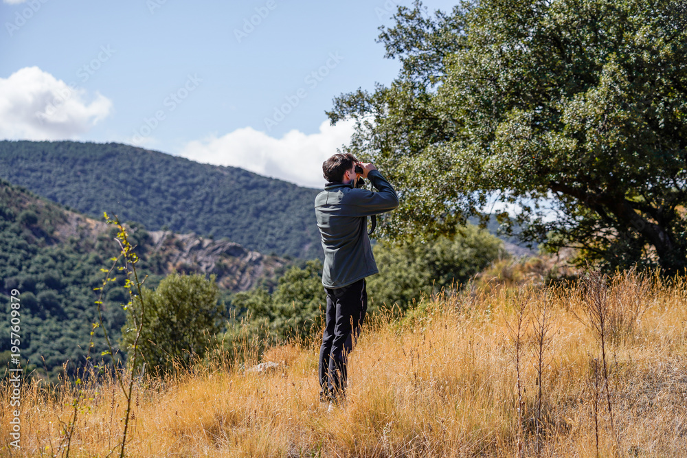 Obraz premium Young man looking at the horizon with binoculars in the forest