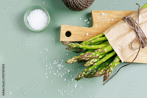Top view of paper-wrapped green asparagus with sea salt and kitchen string on wooden cutting board