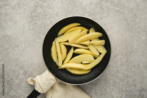 Sliced potatoes in a frying pan on a kitchen counter during cooking session in the afternoon