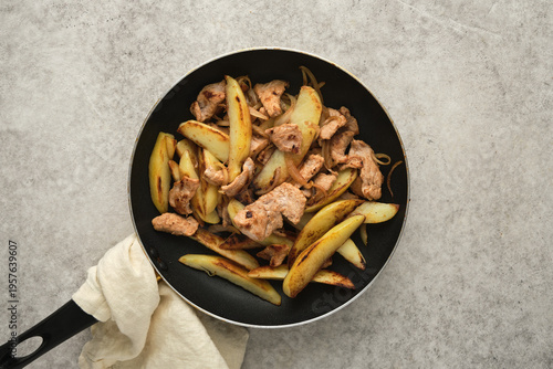 Chicken and potato stir fry in a pan on a gray surface with a towel