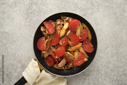 Cooked chicken with tomatoes and potatoes in a frying pan in a kitchen setting during the daytime