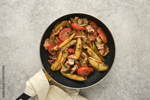 Chicken and potato dish with tomatoes prepared in a frying pan in a kitchen setting during day time