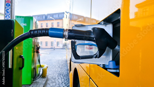 Quadro su tela Yellow city bus refueling at fuel station, side view with nozzle connected