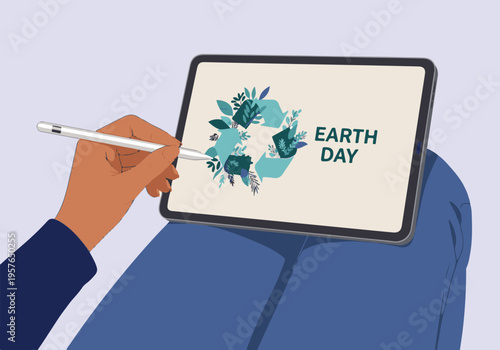 Hand with stylus designing Earth Day recycling logo on a tablet screen