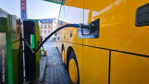 Foto Yellow city bus refueling at fuel station, side view with nozzle connected