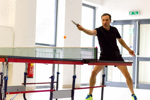 Mid action shot of man returning ball with backhand in table tennis competition.