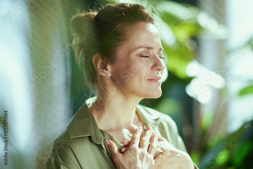 Foto A woman stands peacefully with eyes closed and hands on her chest, finding a quiet moment of reflection and self-care in a lush, natural interior