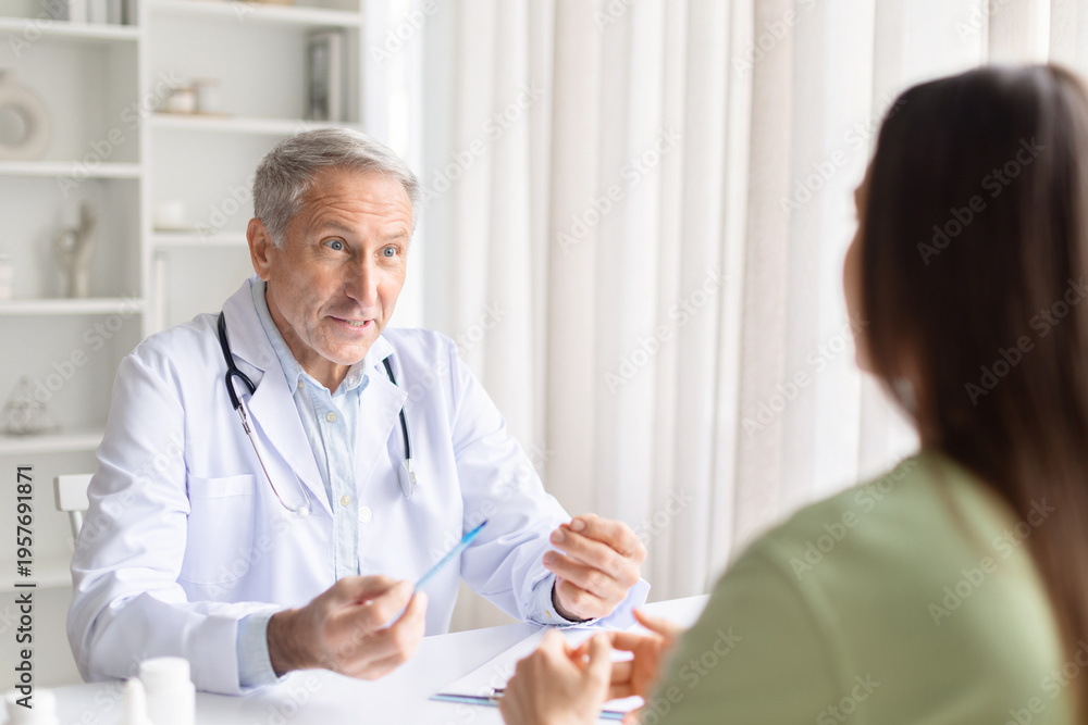 Obraz premium Senior male doctor explaining treatment plan to female patient during clinic consultation. Healthcare professional giving advice and discussing healthcare options