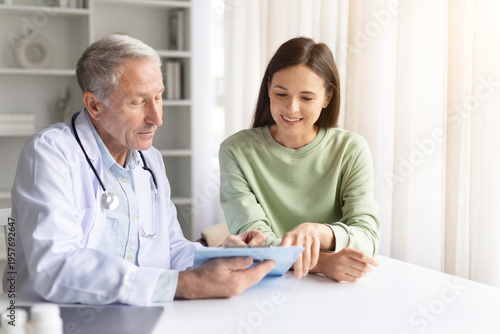 Photos Doctor showing medical information on clipboard to pregnant patient during prenatal consultation