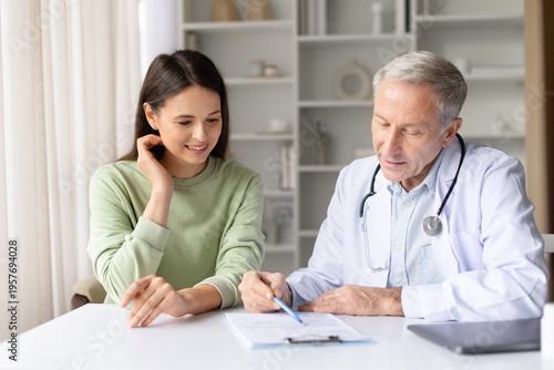 Pregnant woman reviewing medical paperwork with doctor during prenatal consultation. Healthcare professional explaining medical report and pregnancy care