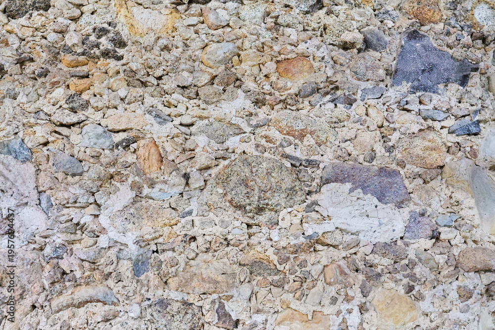 Obraz premium Close-up of an old, rustic stone wall. Irregular, multi-colored rocks and visible mortar form a rough, earthy texture. 