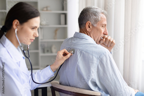 Foto Female doctor examining senior patients lungs with stethoscope on back while patient coughs