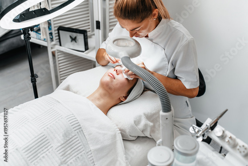 Tableau sur toile Female cosmetologist using magnifying lamp to perform skin cleaning and facial treatment on woman in professional beauty clinic