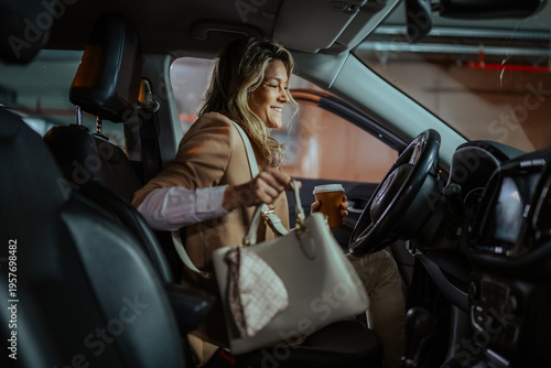 Bilde på lerret Professional woman getting into her car in a parking garage with coffee and a ha