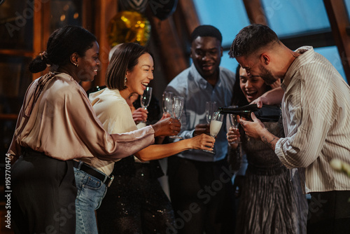 Diverse friends celebrating together, a man pouring champagne into glasses, women smiling and laughing at a social event