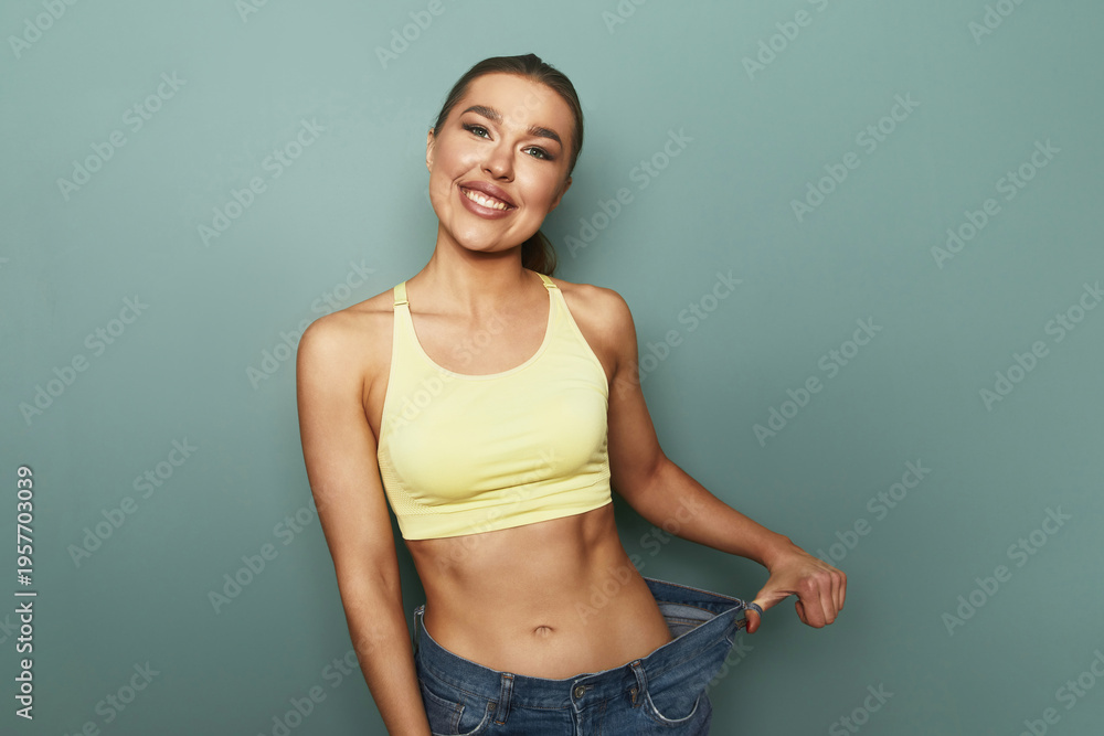 Obraz premium Woman shows excitement after fitting into new jeans in studio against blue wall