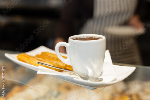 Hot chocolate in a white mug next to a portion of churros close up