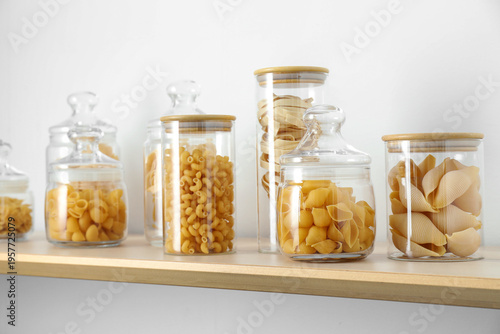 Different types of pasta in jars on wooden shelf