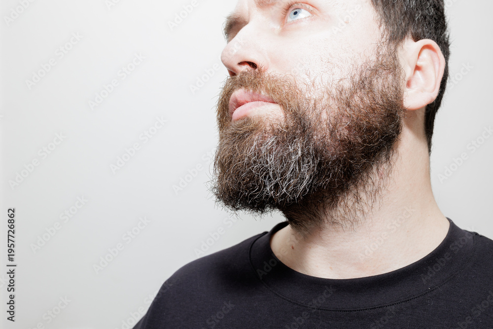 Obraz premium A detailed close-up shot of a man's thick, salt and pepper beard looking upwards against a white background. Stock photo