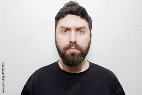 Tableau sur toile A straightforward frontal headshot of a serious man with a thick beard and blue eyes on a white background