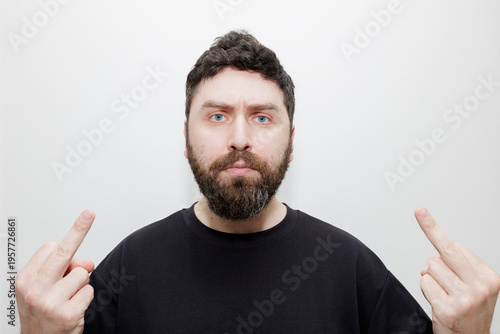 Bild auf Leinwand A portrait of an expressive man with a beard showing the middle finger gesture against a white studio background