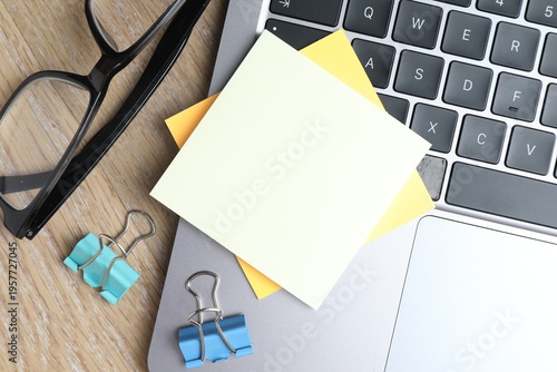 Reminder. Blank sticky notes, laptop, binder clips and glasses on wooden table, flat lay