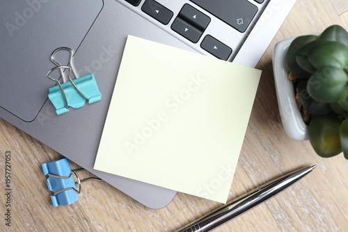 Reminder. Blank sticky note, stationery, laptop and floral decor on wooden table, flat lay