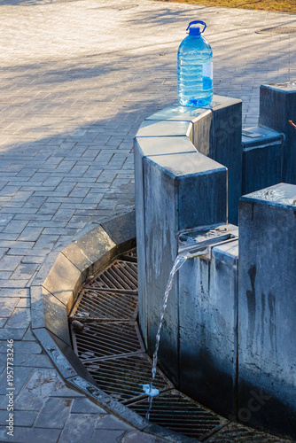 Photography An outdoor drinking fountain with running water and a plastic bottle on a stone pedestal