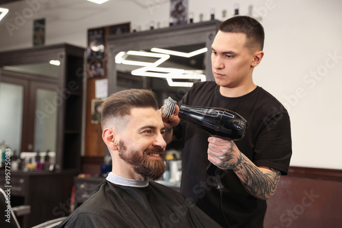 Obraz na płótnie Stylist blow drying man's hair in barbershop
