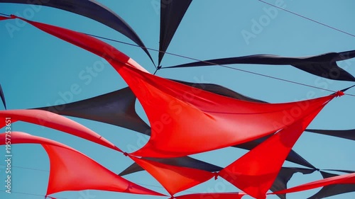 abstract view of red and black triangle shaped cloth decoration waving by wind on blue sky background. summer sea camp or beach club decoration, vibrant colors