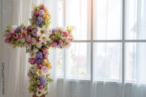Decorative easter cross covered in fresh spring flowers positioned near a large window with sheer curtains, bright airy interior, soft natural light highlighting white petals, clean modern aesthetic,