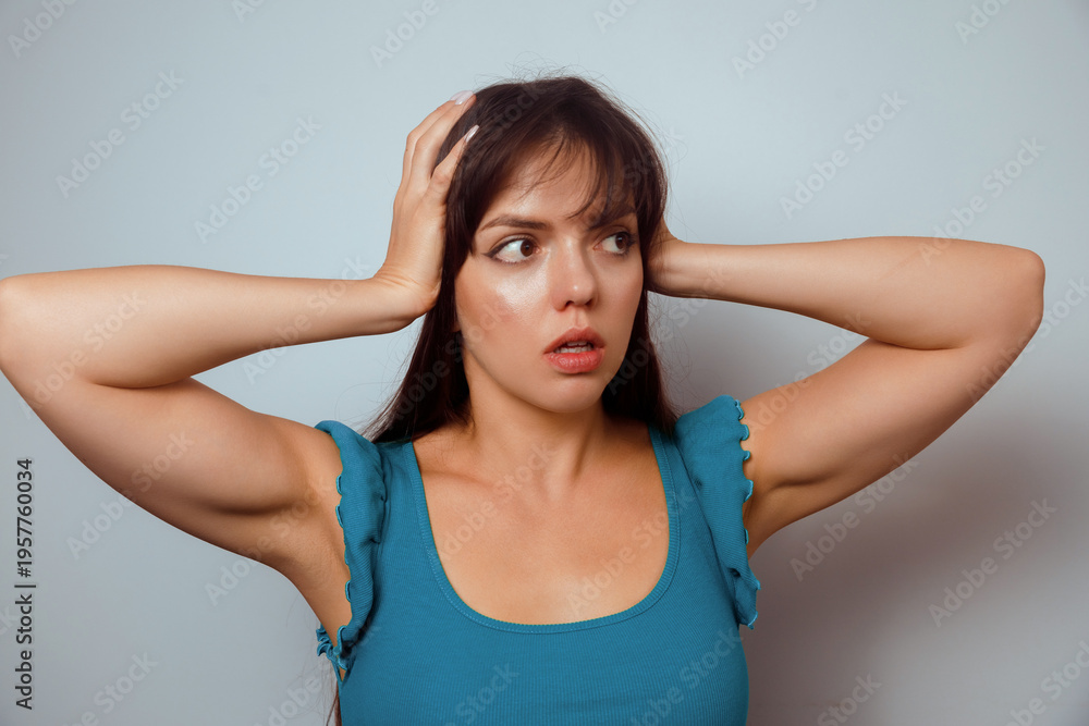 Fototapeta premium Woman shows surprise while touching her hair against a plain background, conveying emotions of shock and curiosity in a beauty-focused lifestyle moment